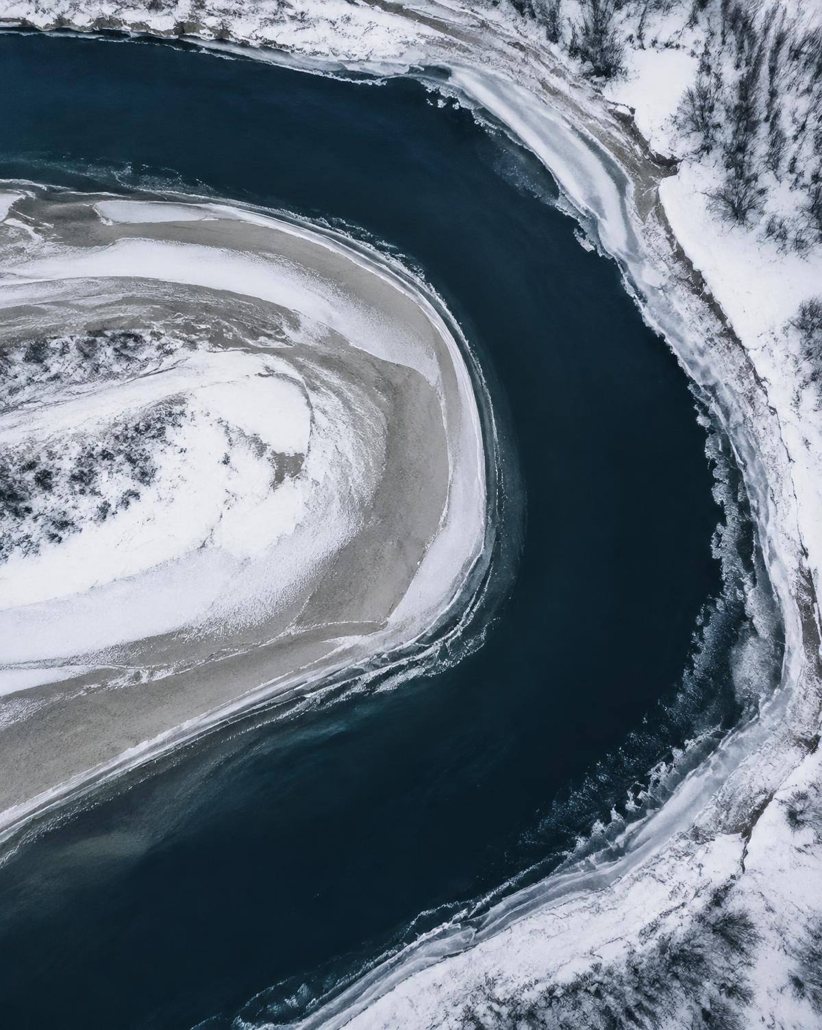 Detail van een rivierbocht tussen sneeuw en zandbank