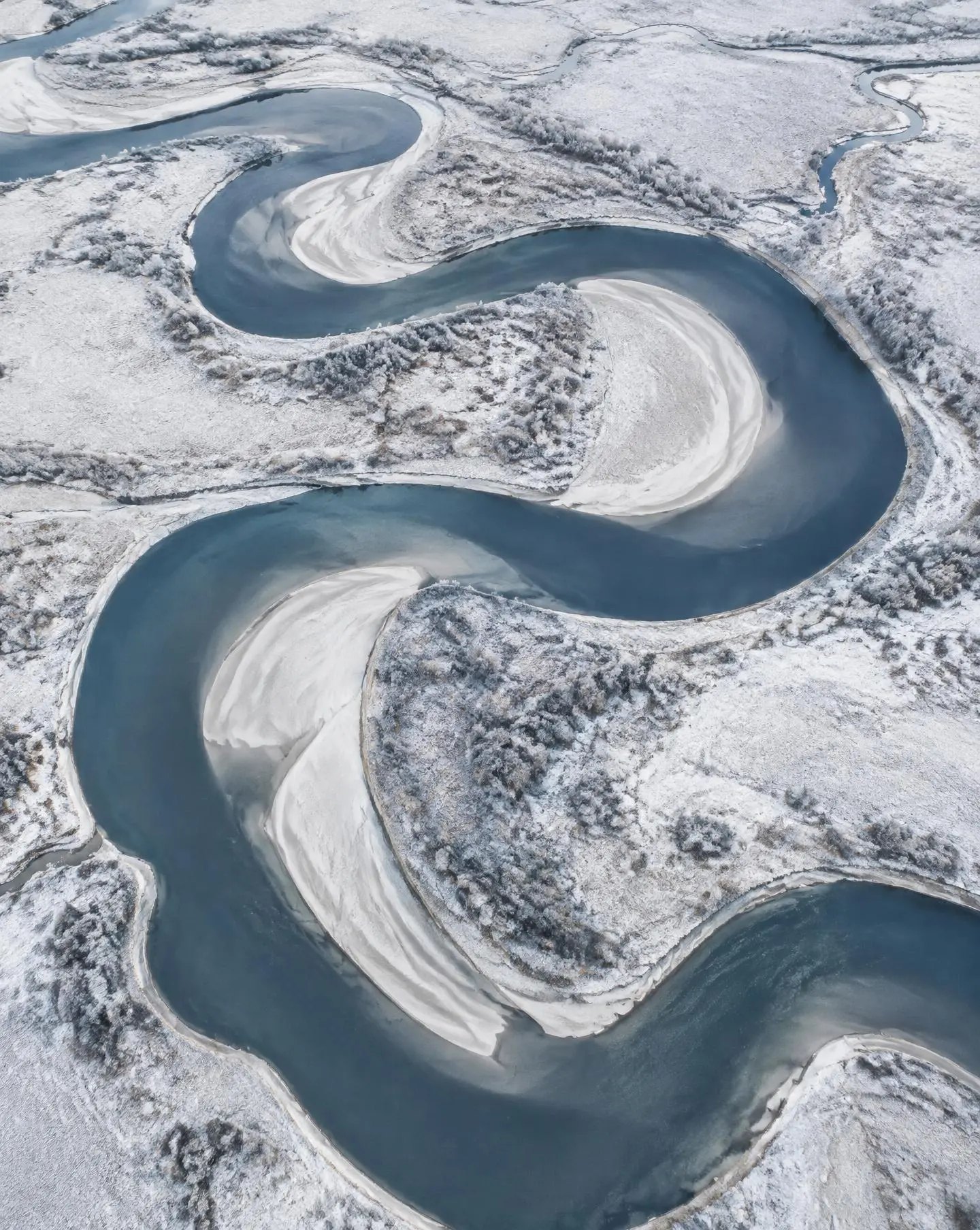 Rivier die in grote S-bochten door een besneeuwd landschap meandert